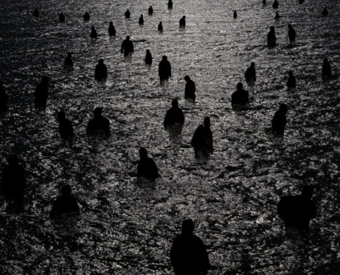 Many dark figures wade in the moonlit water in a black-and-white photo.