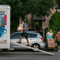 Man carriers cardboard boxes into the back of a Uhaul truck parked in front of a house