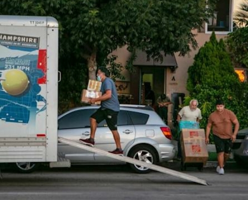 Man carriers cardboard boxes into the back of a Uhaul truck parked in front of a house