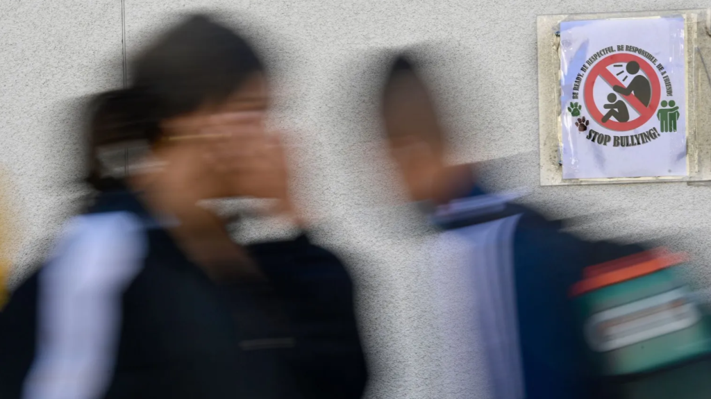 Blurred photo of two students walking by anti-bullying poster in a classroom.