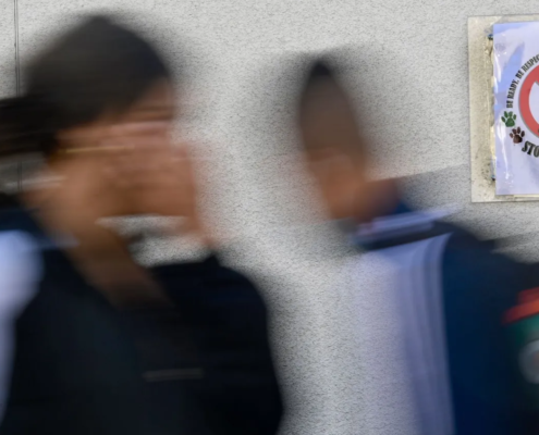 Blurred photo of two students walking by anti-bullying poster in a classroom.