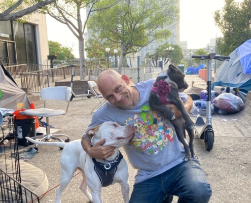Man smiles and poses crouched down with two dogs