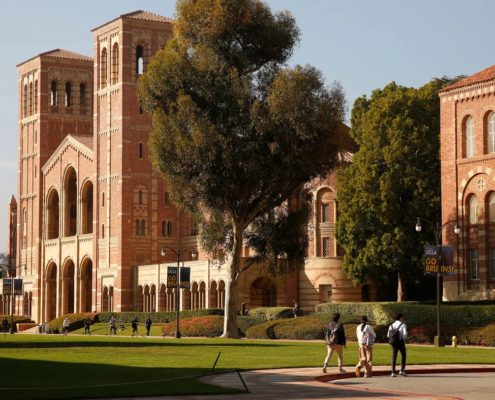 Three students walk across the parking lot on the UCLA campus in front of Royce Hall