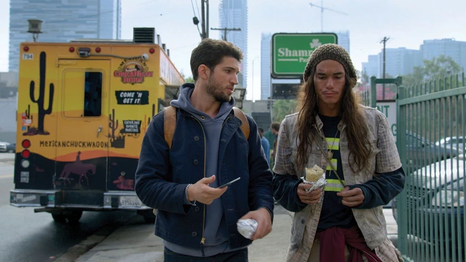 A white man walks next to another white man experiencing homelessness in an image from an episode of the Freeform series 'Good Trouble.'