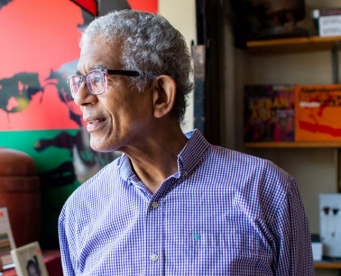 Middle-ahed man wearing glasses and a button-down shirt looks away from the camera in a bookstore.