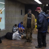 Man in a baseball cap talks to unhoused individuals in a subway station.