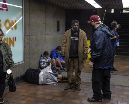 Man in a baseball cap talks to unhoused individuals in a subway station.