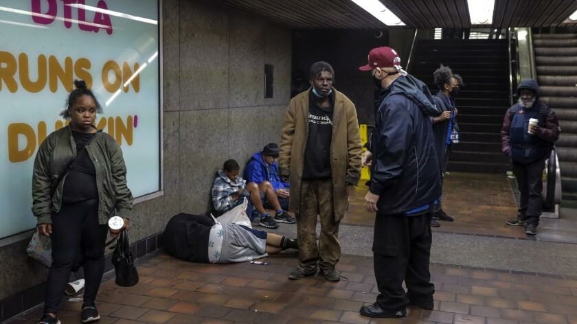 Man in a baseball cap talks to unhoused individuals in a subway station.