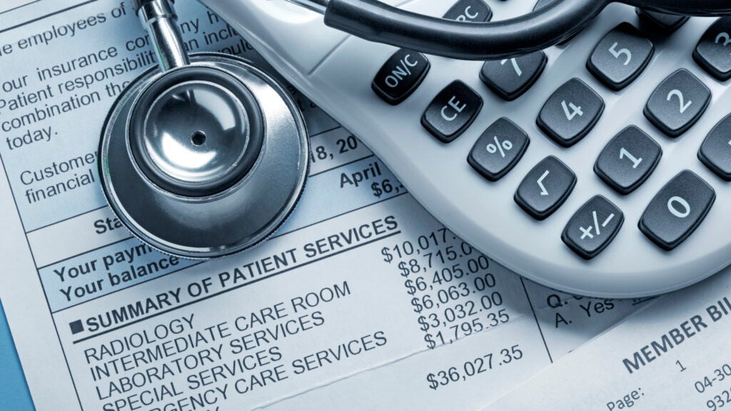 A stethoscope and a calculator rest on top of a medical bill.
