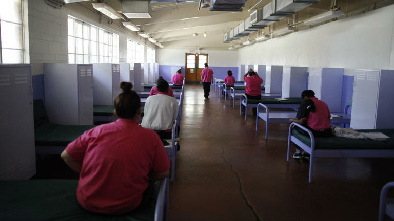 Incarcerated girls at the Camp Scott detention center in Santa Clarita sit on bunks facing away from the camera.