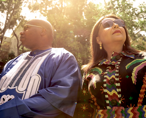 Man in blue attire, woman in multicolored attire sitting outside on sunny day