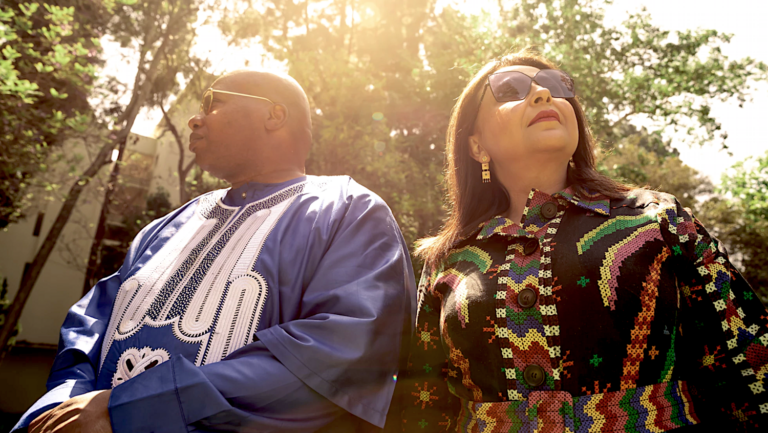 Man in blue attire, woman in multicolored attire sitting outside on sunny day