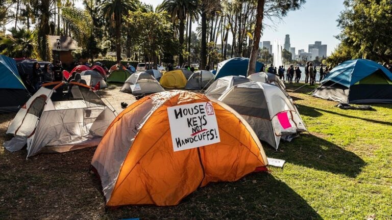 tents in park, with sign reading "House Keys Not Handcuffs"