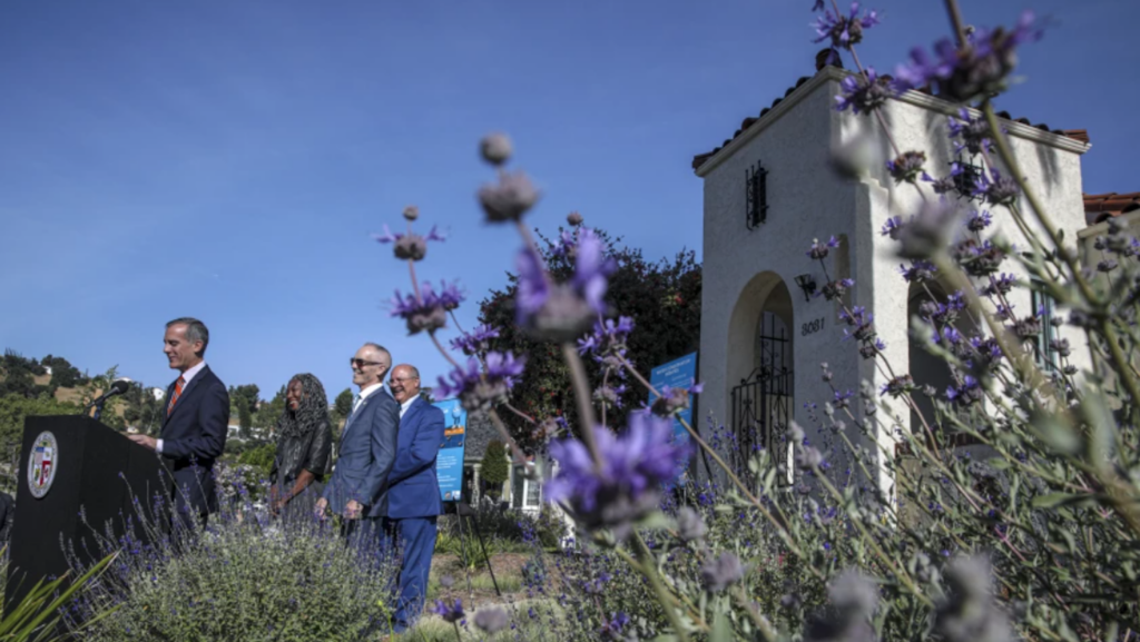 three men, one woman speaking in garden with purple sage