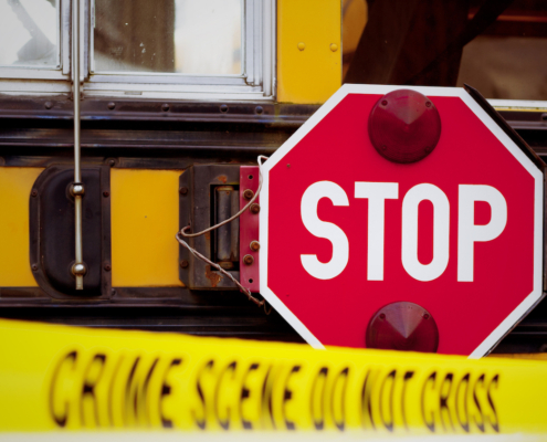 The side of a school bus with cordon tape that reads "CRIME SCENE DO NOT CROSS".