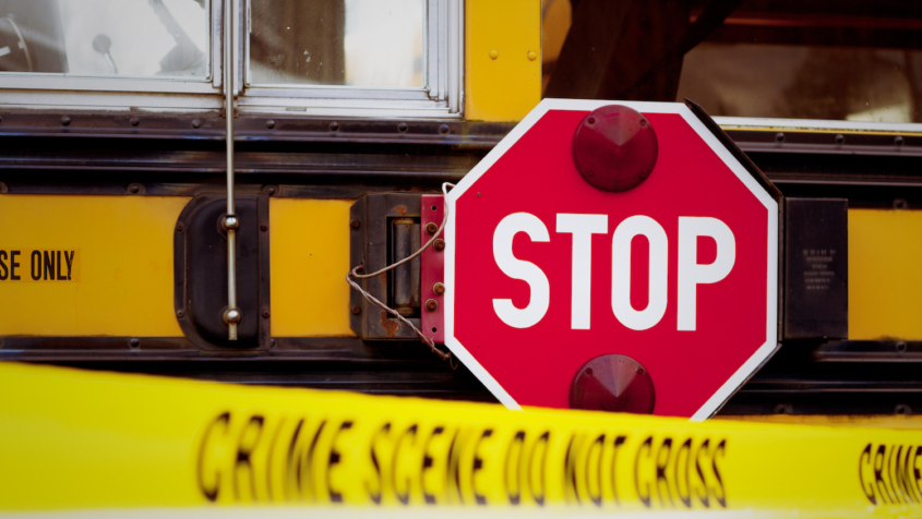 The side of a school bus with cordon tape that reads "CRIME SCENE DO NOT CROSS".