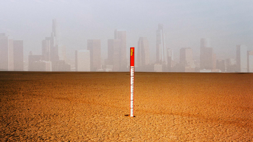Thermometer in the desert with city buildings in the background