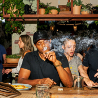 A man in a black T-shirt and baseball cap smokes a joint while sitting at the counter of a weed cafe in California.