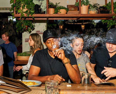 A man in a black T-shirt and baseball cap smokes a joint while sitting at the counter of a weed cafe in California.
