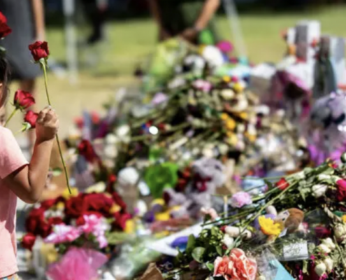 A young girl carries roses in one hand to place at a memorial for the victims of a school shooting at Robb Elementary School in Uvalde, Texas.