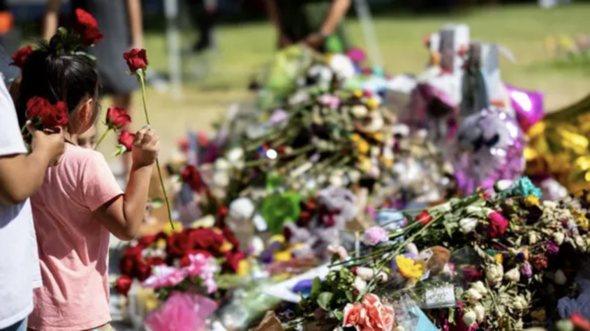 A young girl carries roses in one hand to place at a memorial for the victims of a school shooting at Robb Elementary School in Uvalde, Texas.