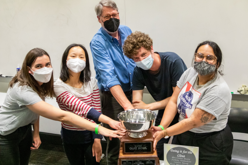 four students and a professor touch the trophy given to the winning team