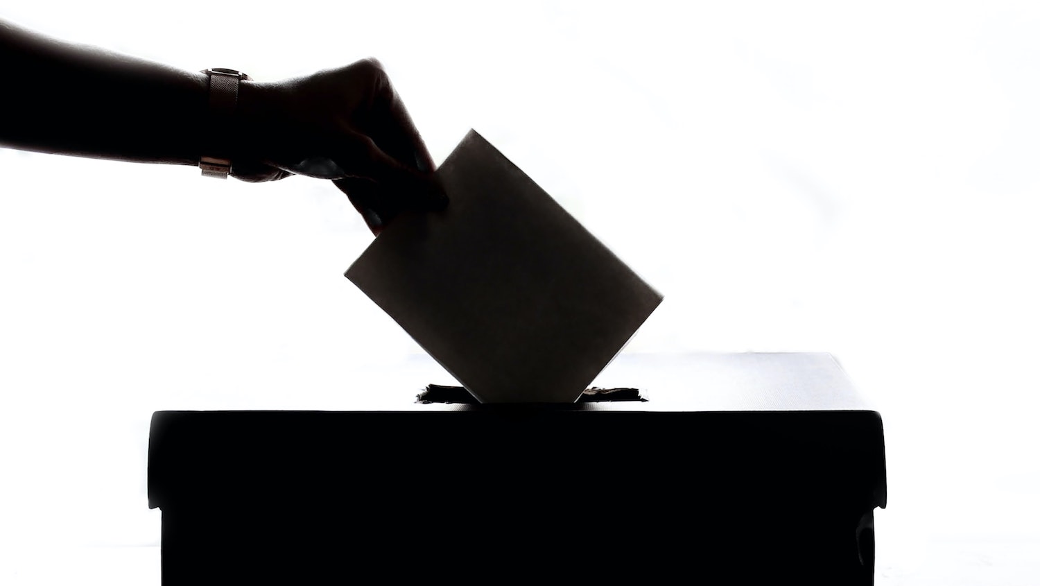 silhouette of hand placing ballot into box