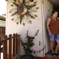 A mother and her daughter lean against the doorframe of their front door on a hot day.