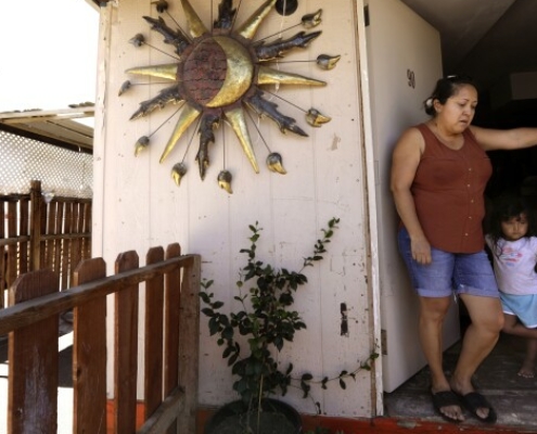A mother and her daughter lean against the doorframe of their front door on a hot day.
