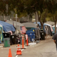 A man walks along the road next to a cluster of tents at a homeless encampment.