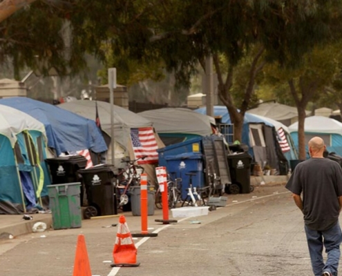 A man walks along the road next to a cluster of tents at a homeless encampment.