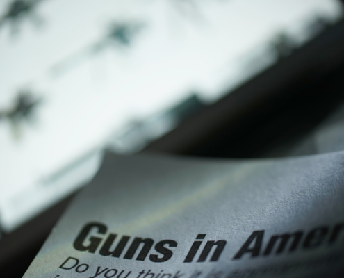 paper shows text reading guns in America in front of a bright screen with images of firearms