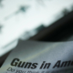 paper shows text reading guns in America in front of a bright screen with images of firearms