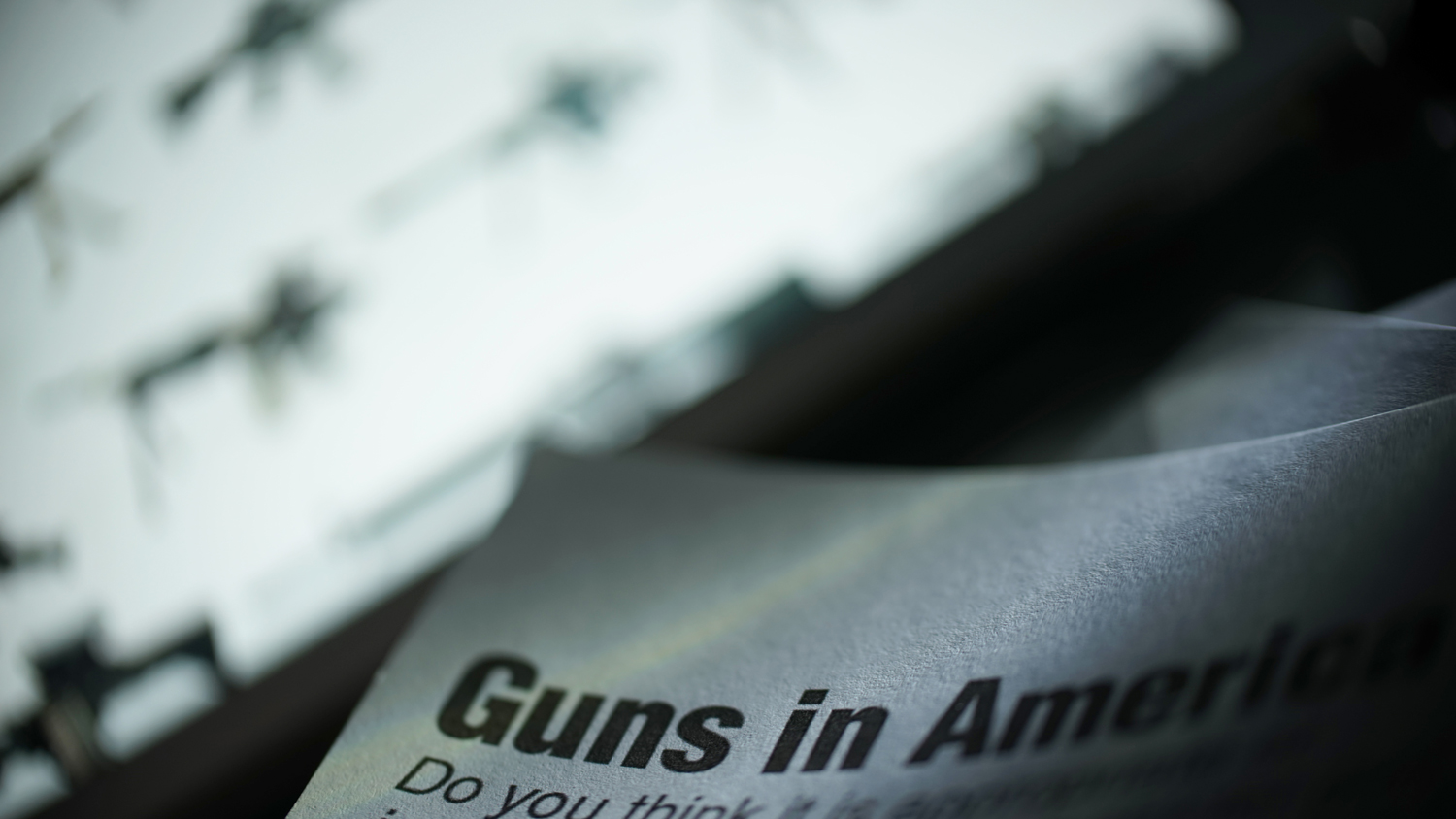 paper shows text reading guns in America in front of a bright screen with images of firearms