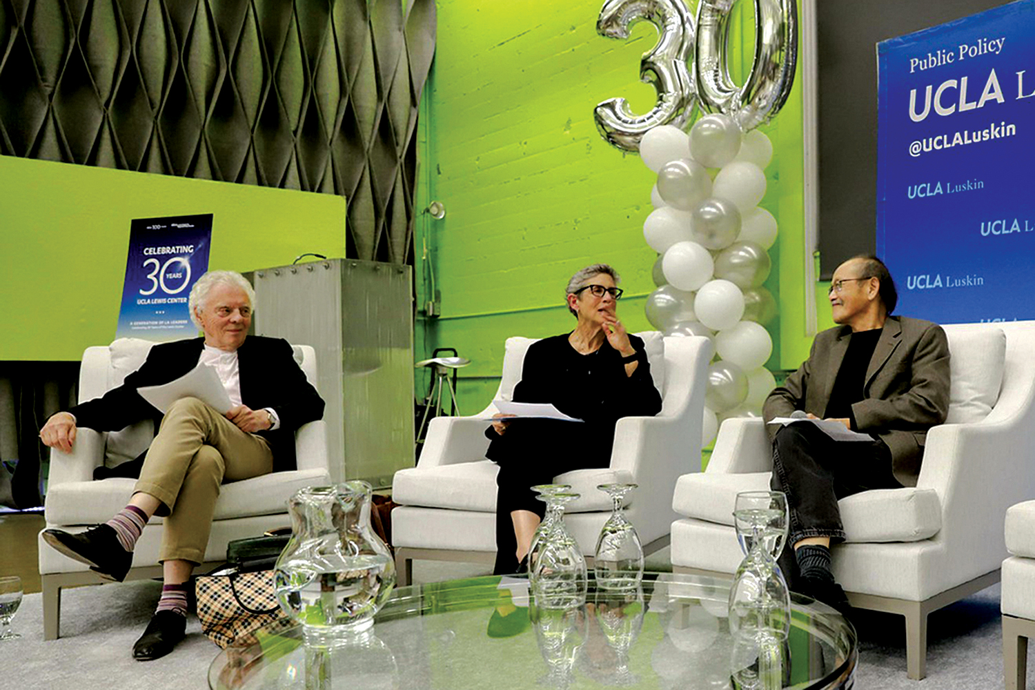 two men and a woman sit in large white chairs and talk