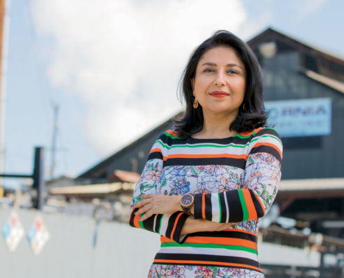 woman stands with arms crossed in foreground and building in distance
