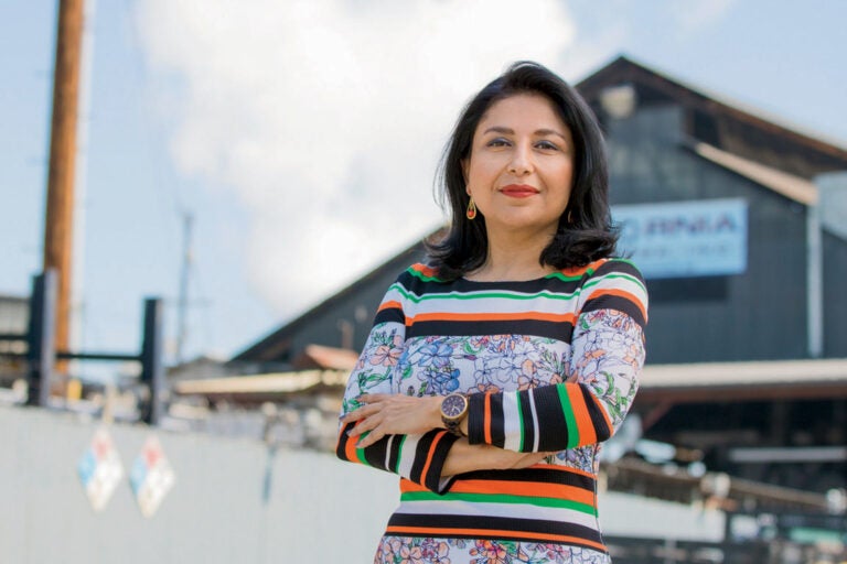 woman stands with arms crossed in foreground and building in distance