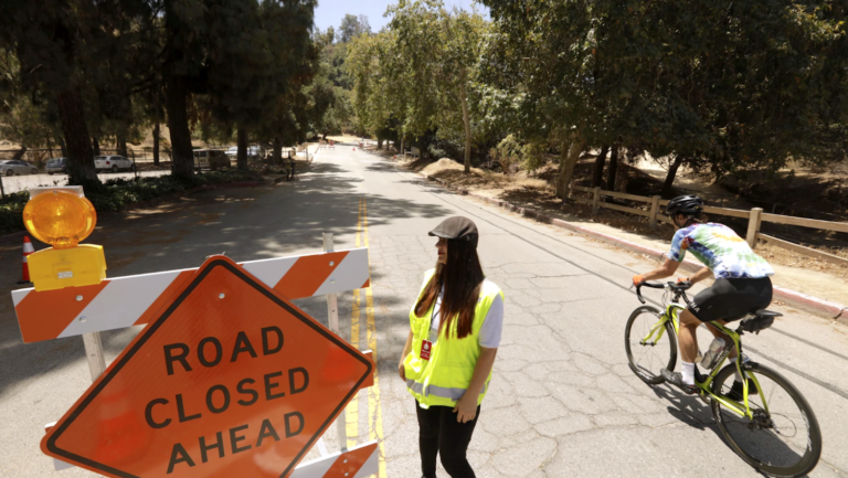 bicyclist on wooded road next to road closure sign and woman in yellow safety vest