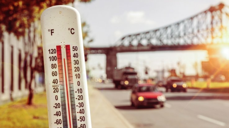 Thermometer reads 100 degrees Fahrenheit with cars driving on a street in the background