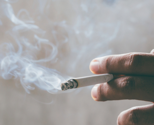 Hand holding lit cigarette and showing smoke