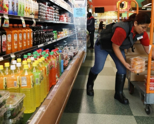 woman stocks refrigerator case at grocery story