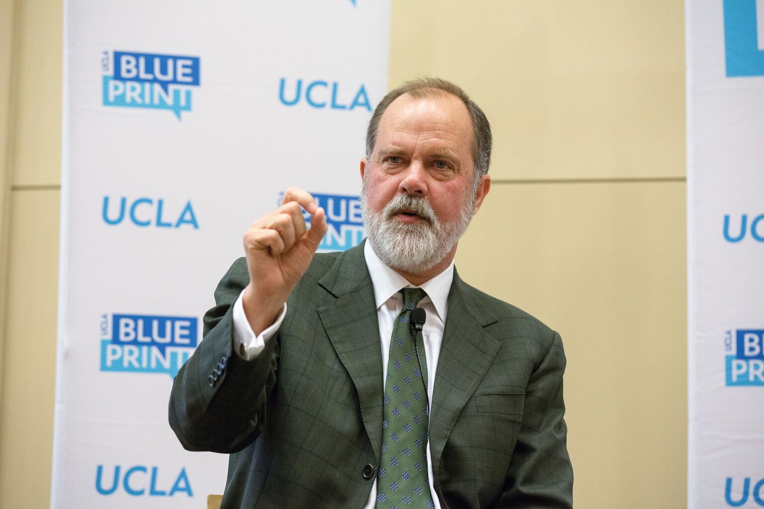 main in suit and tie gestures in front of backdrop showing UCLA and Blueprint logos|