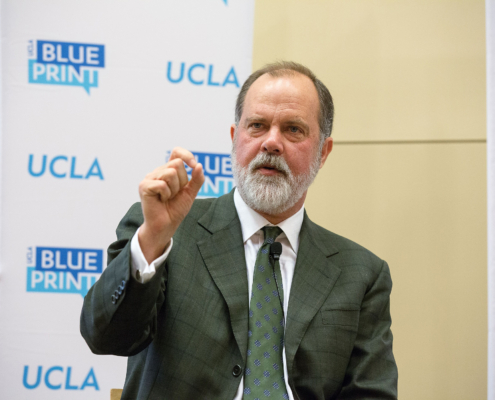 main in suit and tie gestures in front of backdrop showing UCLA and Blueprint logos