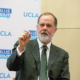 main in suit and tie gestures in front of backdrop showing UCLA and Blueprint logos