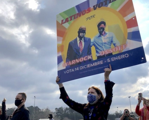 woman in mask holding multicolored sign to get out the vote