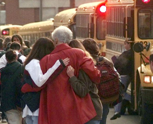 school crowd including woman in red coat hugging two girls in front of school bus