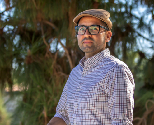 Man in cap and glasses outdoors in front of trees