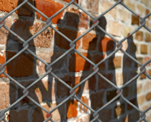 Shadows of people on a wall behind a fence