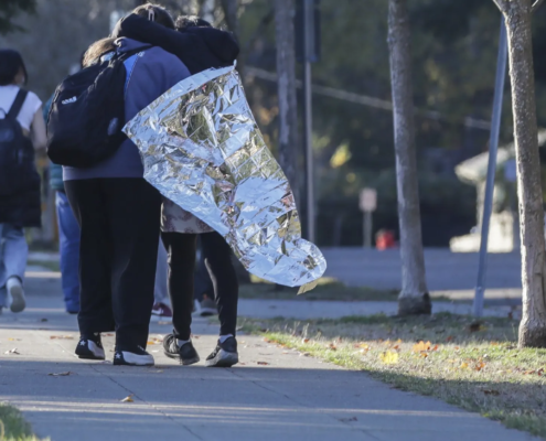 two people on sidewalk, one wrapped in metallic blanket