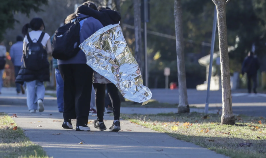 two people on sidewalk, one wrapped in metallic blanket